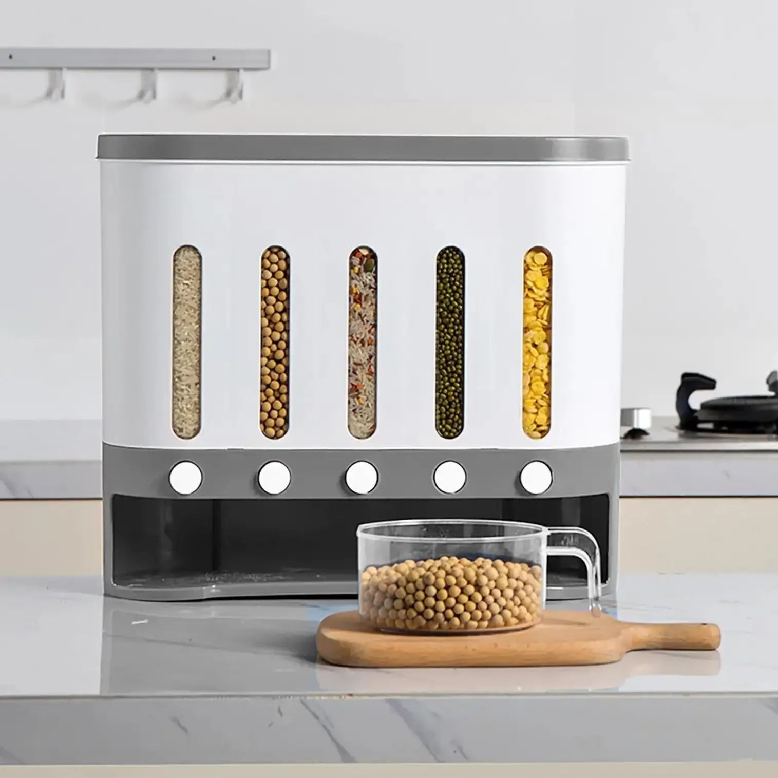 The Cereal Dispenser with its 5 grids full, Resting on a kitchen bench top with a plastic jug full of grains on a chop board sitting in front