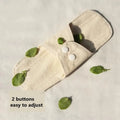 A Reusable Sanitary Pad with its wings folded in and buttoned up, tiny leaves resting on and around the pad.