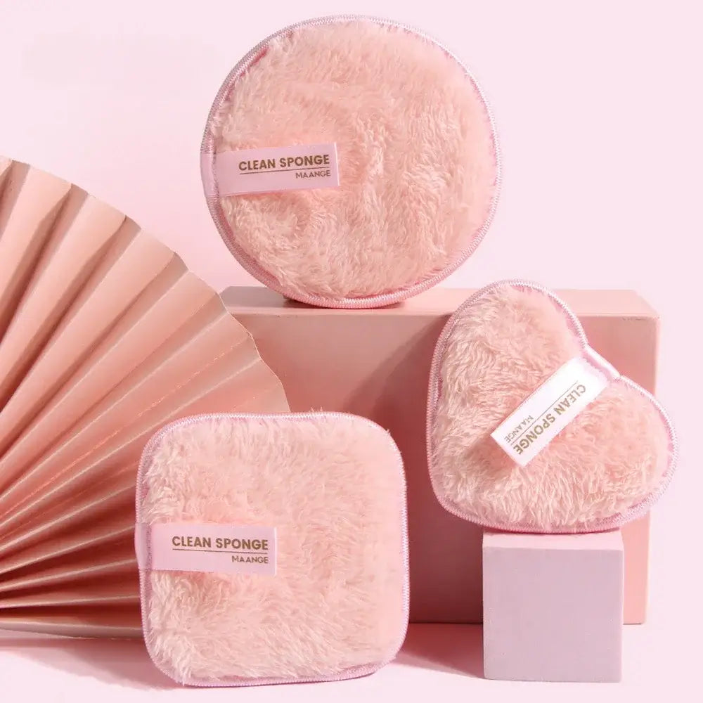 The 3 reusable makeup remover pads, 2 on top of Pink boxes and 1 on the floor. A pink hand held fan to the left with a pink background